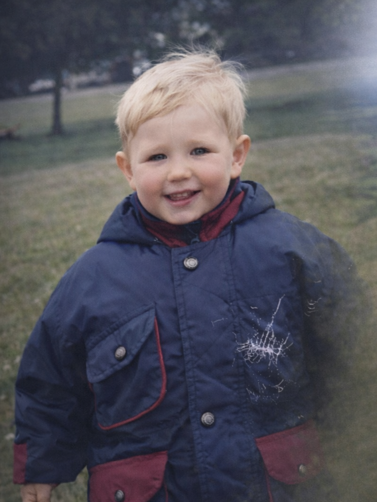 Me as a small child, smiling in a navy and red coat